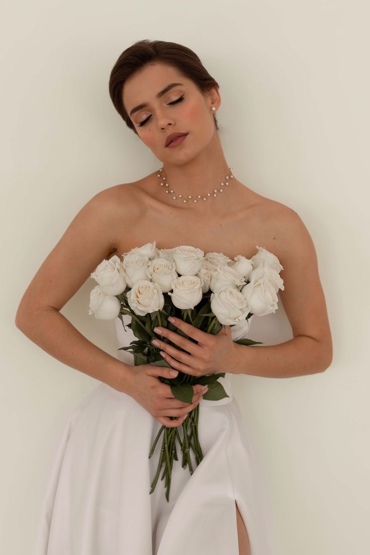 a woman in a white dress holding a bouquet of flowers with her hands behind her back