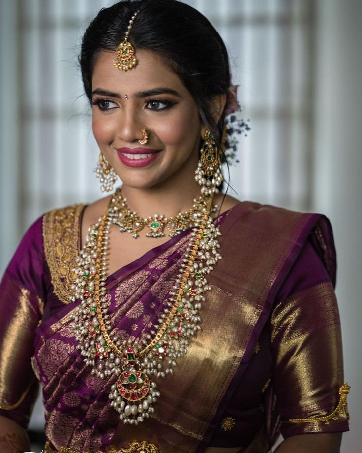 a woman in a purple and gold sari with jewelry on her neck, smiling