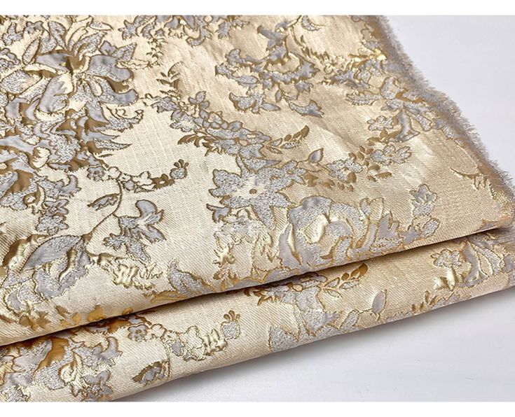 two pieces of gold brocaded fabric with silver flowers and leaves on white background