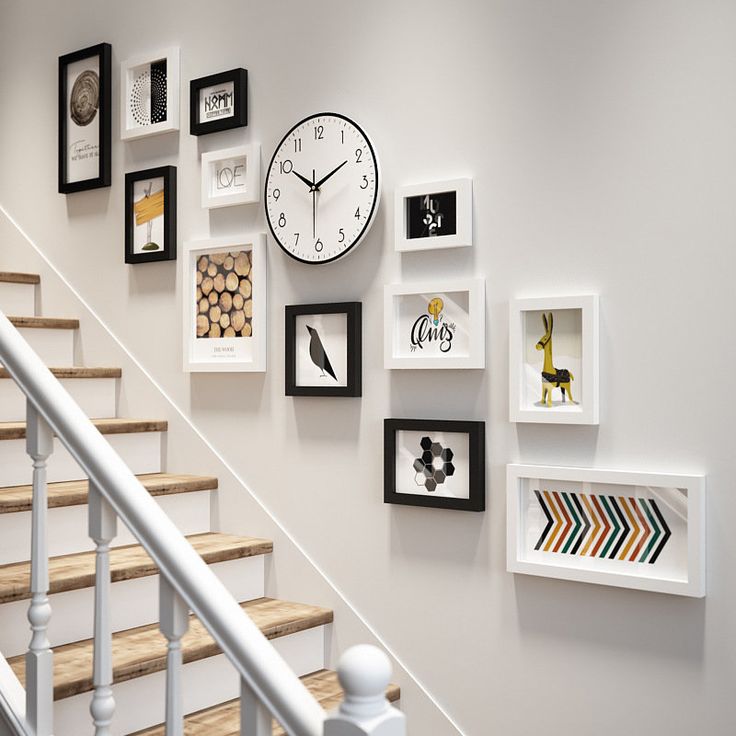 a wall with many different pictures on it and a clock mounted to the wall next to some stairs