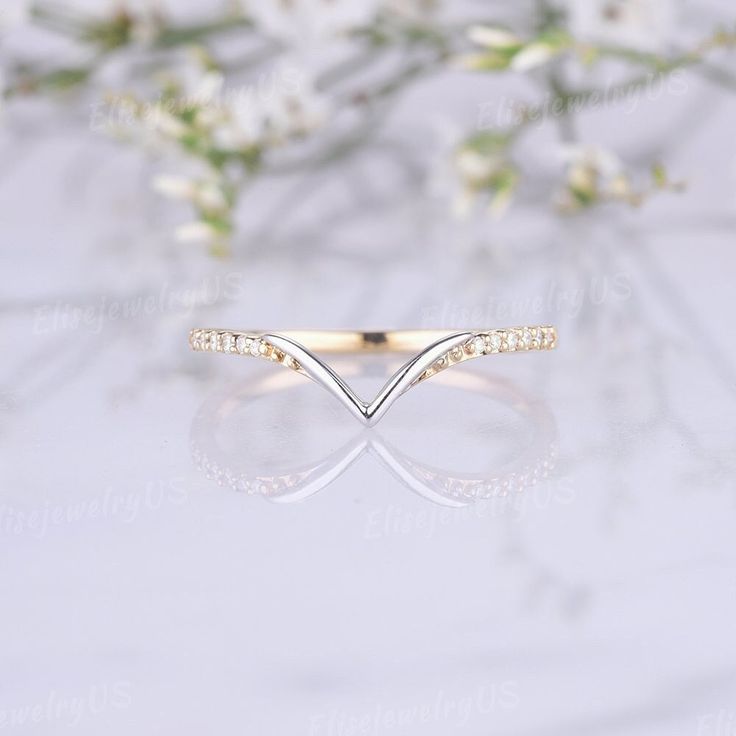 a gold ring with white diamonds on it and some flowers in the background, sitting on top of a table