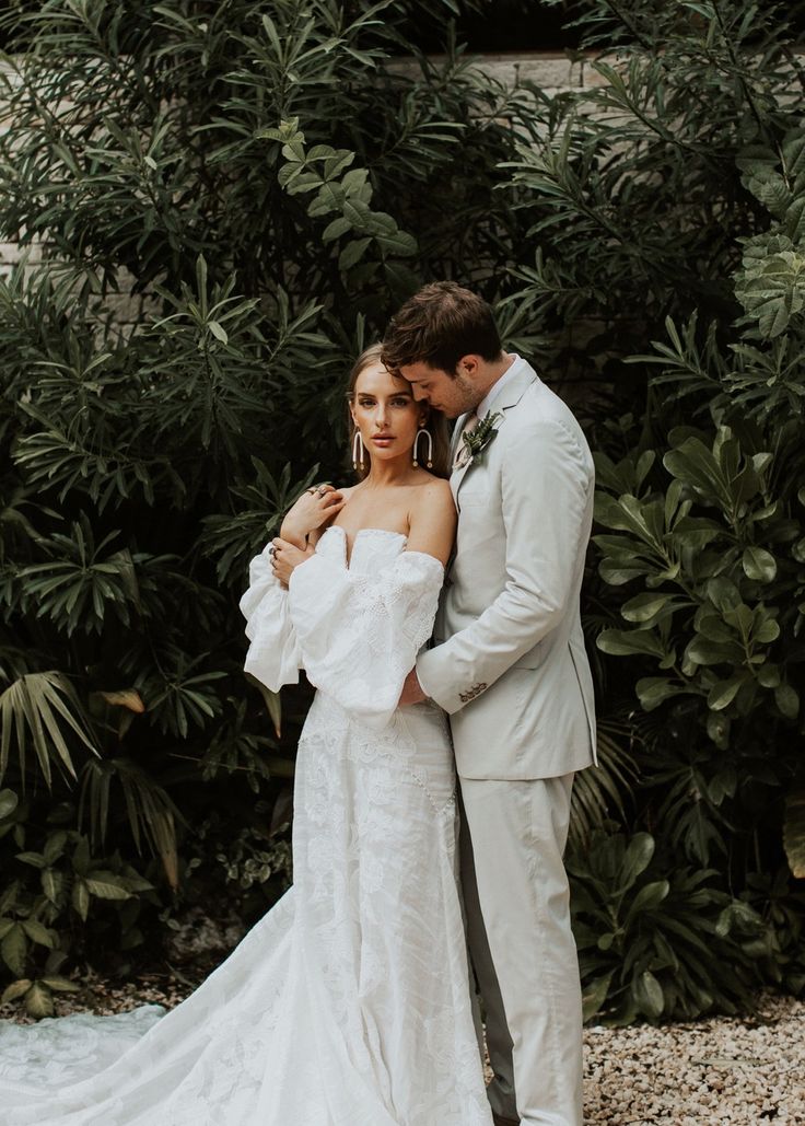 a bride and groom are standing in front of some trees with their arms around each other