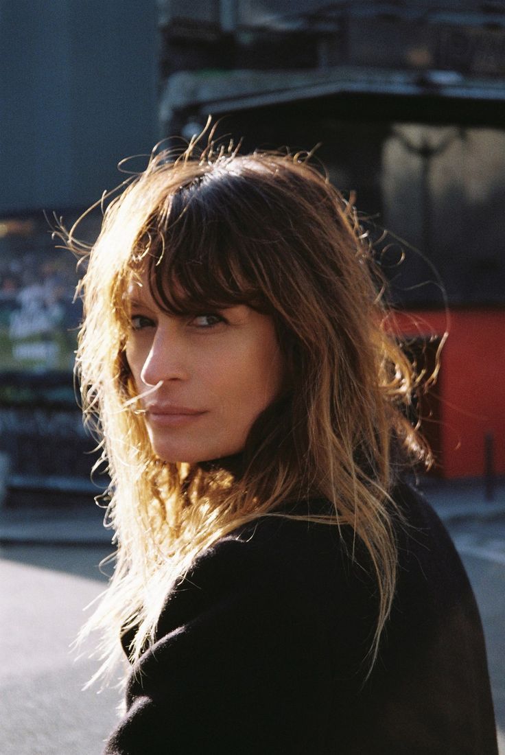 a woman standing in front of a bus on the street with long hair and blue eyes