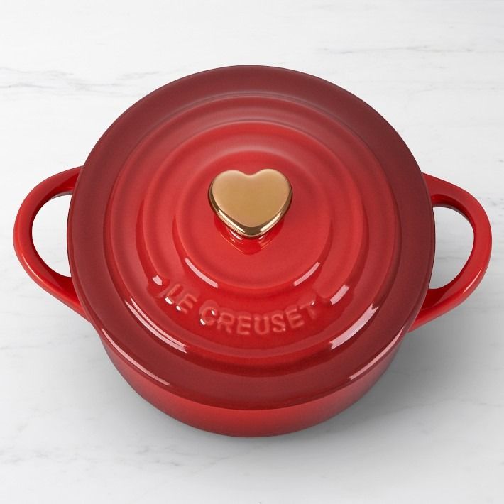 a red casserole with a gold heart on the lid is sitting on a marble surface