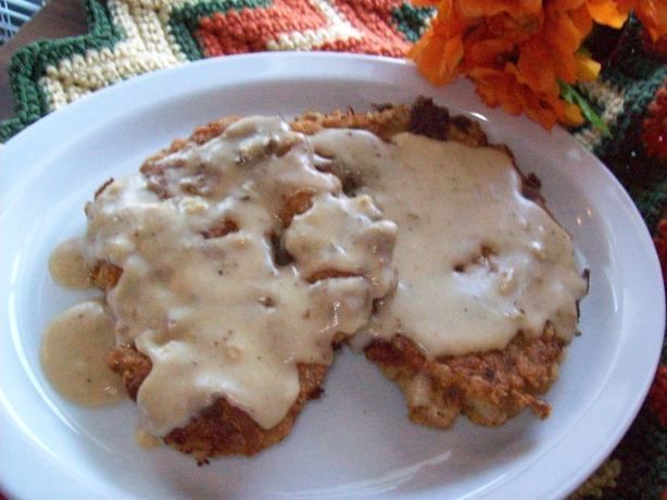 two pieces of meat covered in gravy on a white plate next to orange flowers