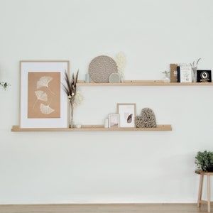 two wooden shelves with pictures, plants and other items on them against a white wall