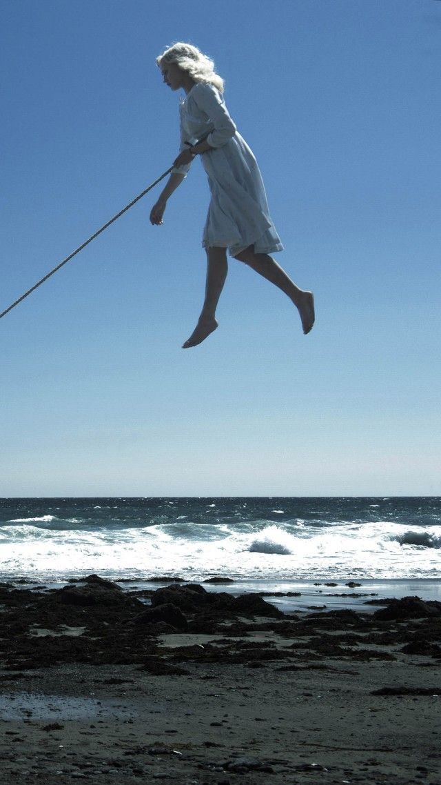 a woman jumping in the air on top of a beach