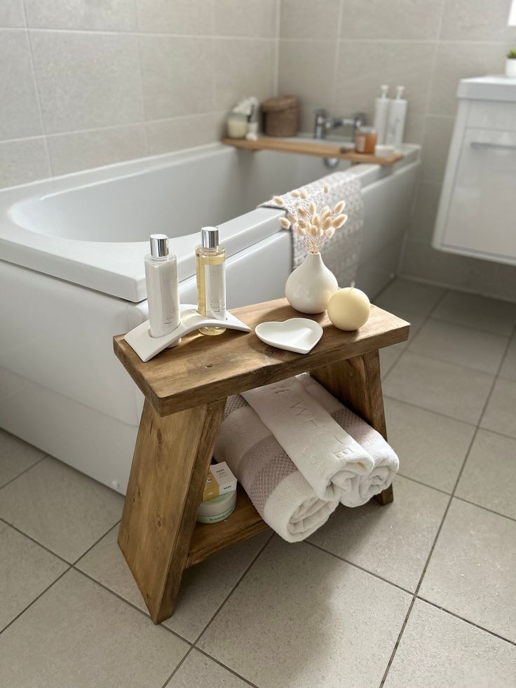 a white bath tub sitting next to a wooden table with towels on top of it