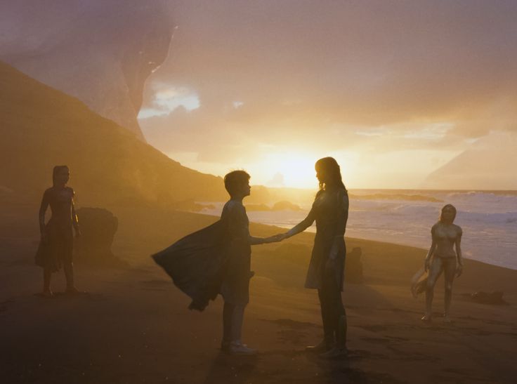 two people shaking hands on the beach as the sun goes down in the distance behind them