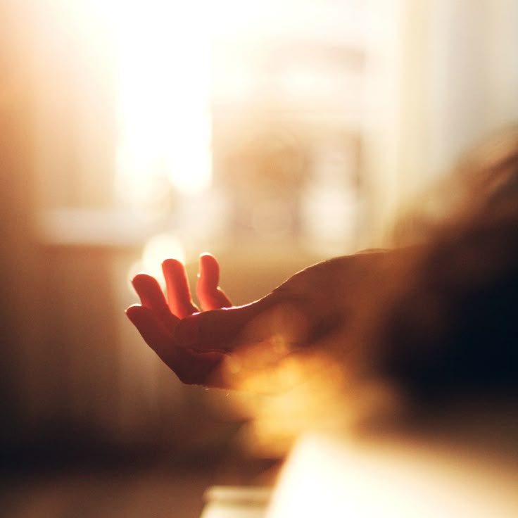 a blurry image of someone's hand reaching out to touch the light coming through them