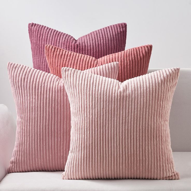 three pink and purple pillows sitting on top of a white couch next to each other