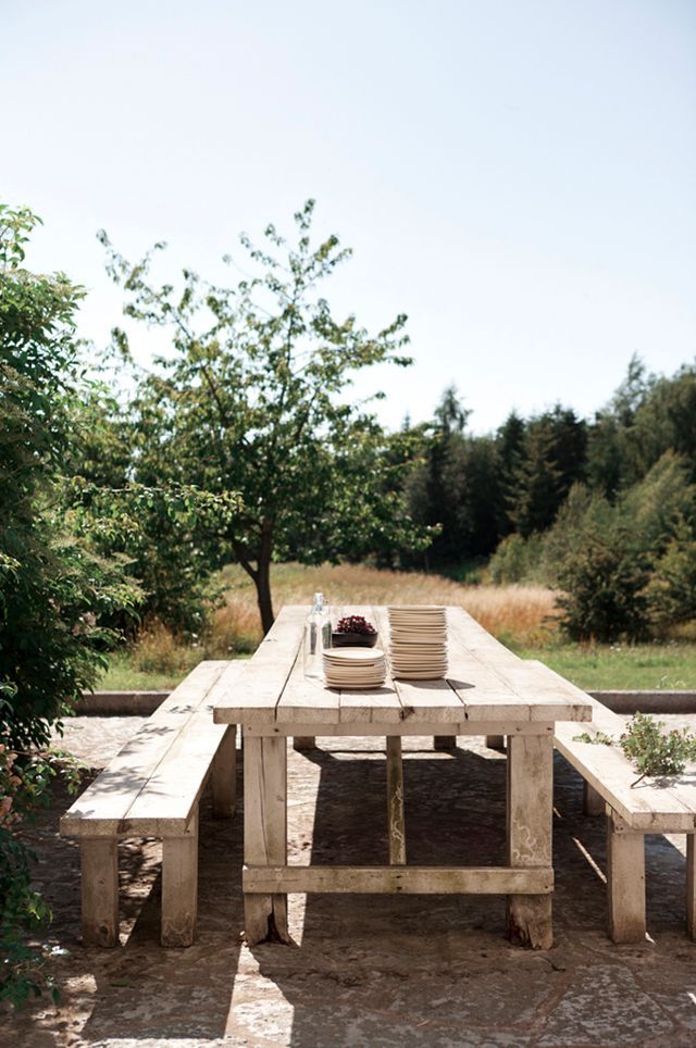 a wooden table with two benches next to it in the middle of a field and trees