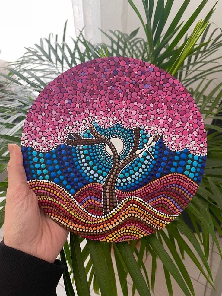 a hand holding up a painted rock with a tree on it