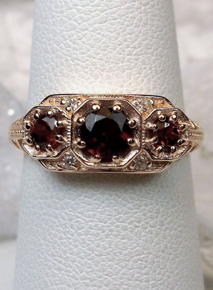 Natural Red Garnet Ring Description  Dainty 3Stone Design#161 Custom This is a high-quality Edwardian reproduction filigree ring in 14K rose gold. This filigree 3 stone ring is set with 3 genuine natural red garnet gemstones. The oval full cut red garnet in the center is 4.5mm. The 2 garnets on each side are 2.5mm. The face of the ring is 15.5mm (5/8th") east-west on the finger and 7mm (1/4th") north-south on the finger. The inside of the band is marked 14K for gold. Notice the beautiful filigre Red Garnet Jewelry, Rose Gold Art, Art Deco Filigree, Red Garnet Ring, Garnet Jewelry, Gold Art Deco, Garnet Ring, Rose Gold Band, North South