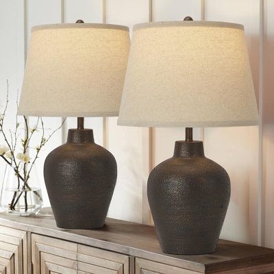 two brown vases sitting on top of a wooden table next to a white lamp