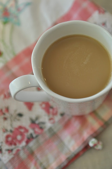 a cup of coffee sitting on top of a flowered table cloth next to a spoon