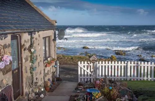 a house next to the ocean with a white picket fence and blue sky in the background