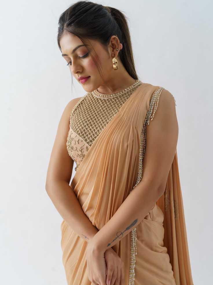 A two-piece peach saree set from the Suruchi Parakh collection. This beautiful pre drape saree is paired with a hand-crafted blouse. The pallu of the pre draped saree has hanging tassels to it. The peach color touch enhances the graceful georgette crepe pre drape saree. The peach blouse has a crew neckline along with geometrical & floral handwork detail. Elegant Peach Designer Wear Blouse Piece, Peach Saree With Dupatta In Traditional Drape, Elegant Peach Sets For Diwali, Peach Blouse Piece With Cutdana Traditional Drape, Peach Unstitched Blouse Piece For Navratri, Unstitched Peach Blouse Piece For Navratri, Peach Saree With Self Design And Traditional Drape, Unstitched Peach Blouse Piece For Diwali, Peach Saree With Self Design In Traditional Drape