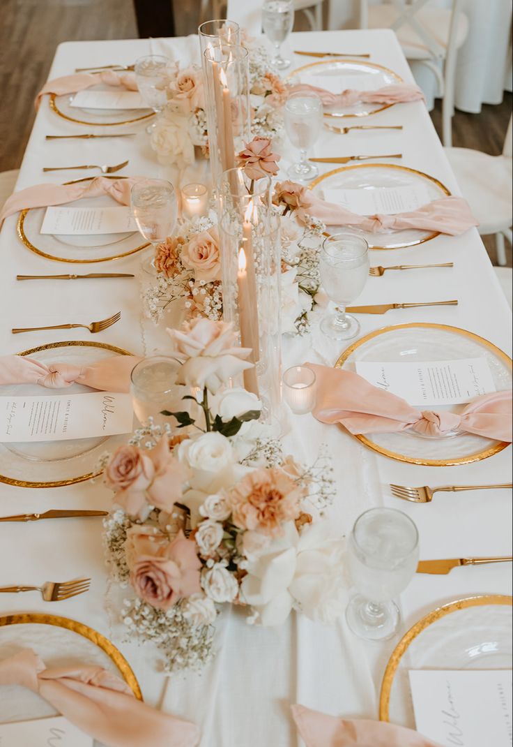 the table is set with white and gold plates, pink napkins, and flowers