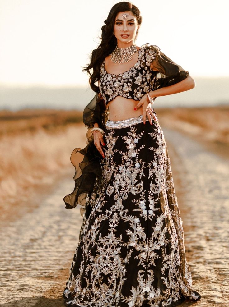 Imani - Black Organza Reception Lehnga with heavy silver zardosi and sequins work Break the stereotype this season and embrace your true desire in this rule-breaking attire perfect for your wedding functions! Scoop neckline choli blouse with Cap sleeve detail & Zardosi handwork Princess cut patterning done to give you the perfect kind of fitting Illusion scoop neck detail accentuates your shoulder line Scallop like trimmed hemline runs all along the neckline & hem adding an interesting d Glamorous Semi-stitched Hand Embellished Choli, Glamorous Choli With Mirror Work For Reception, Glamorous Festive Choli With Intricate Embroidery, Glamorous Designer Lehenga With Intricate Embroidery, Glamorous Lehenga With Unstitched Blouse For Designer Wear, Glamorous Semi-stitched Choli With Zari Work, Glamorous Semi-stitched Choli For Designer Wear, Festive Glamorous Choli With Zari Work, Glamorous Fitted Anarkali Set With Intricate Embroidery