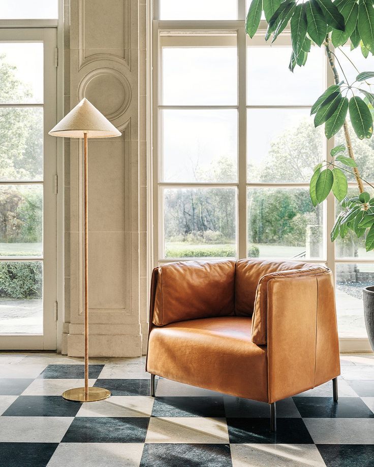 a brown leather chair sitting in front of a window next to a potted plant