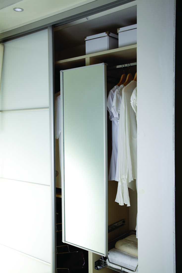 an open closet with clothes on hangers and white cupboards in the corner next to it