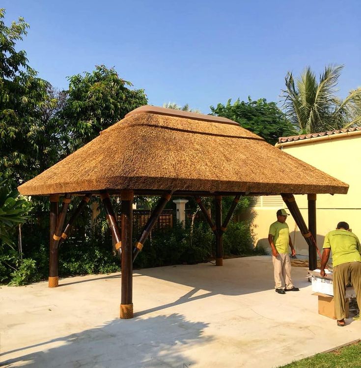 two men standing under a thatch covered gazebo