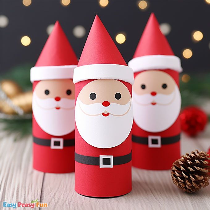 three paper santa clauss sitting next to a pine cone