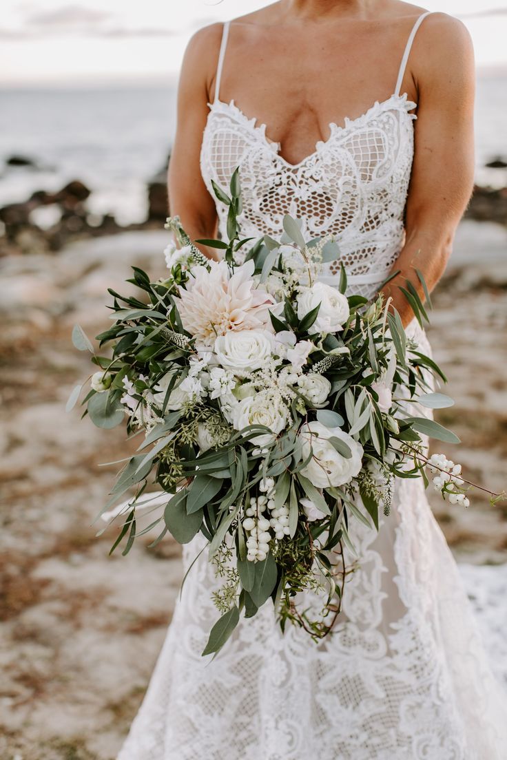 a woman in a wedding dress holding a bridal bouquet with white flowers and greenery