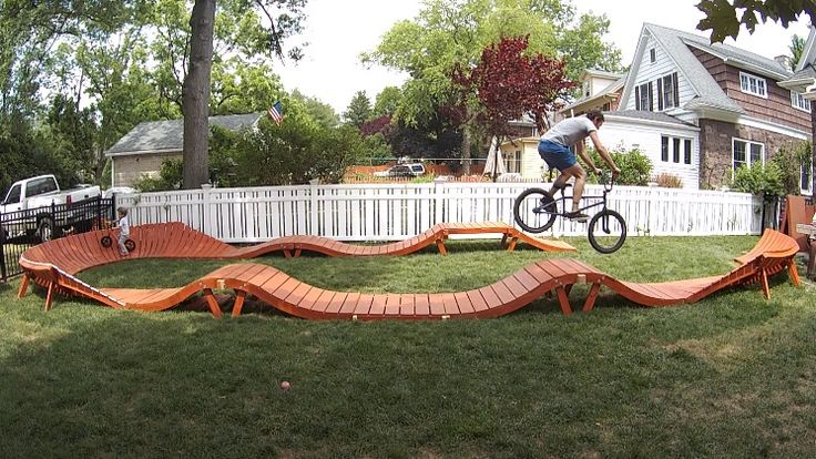 a man riding a bike over a wooden ramp on top of a lush green field