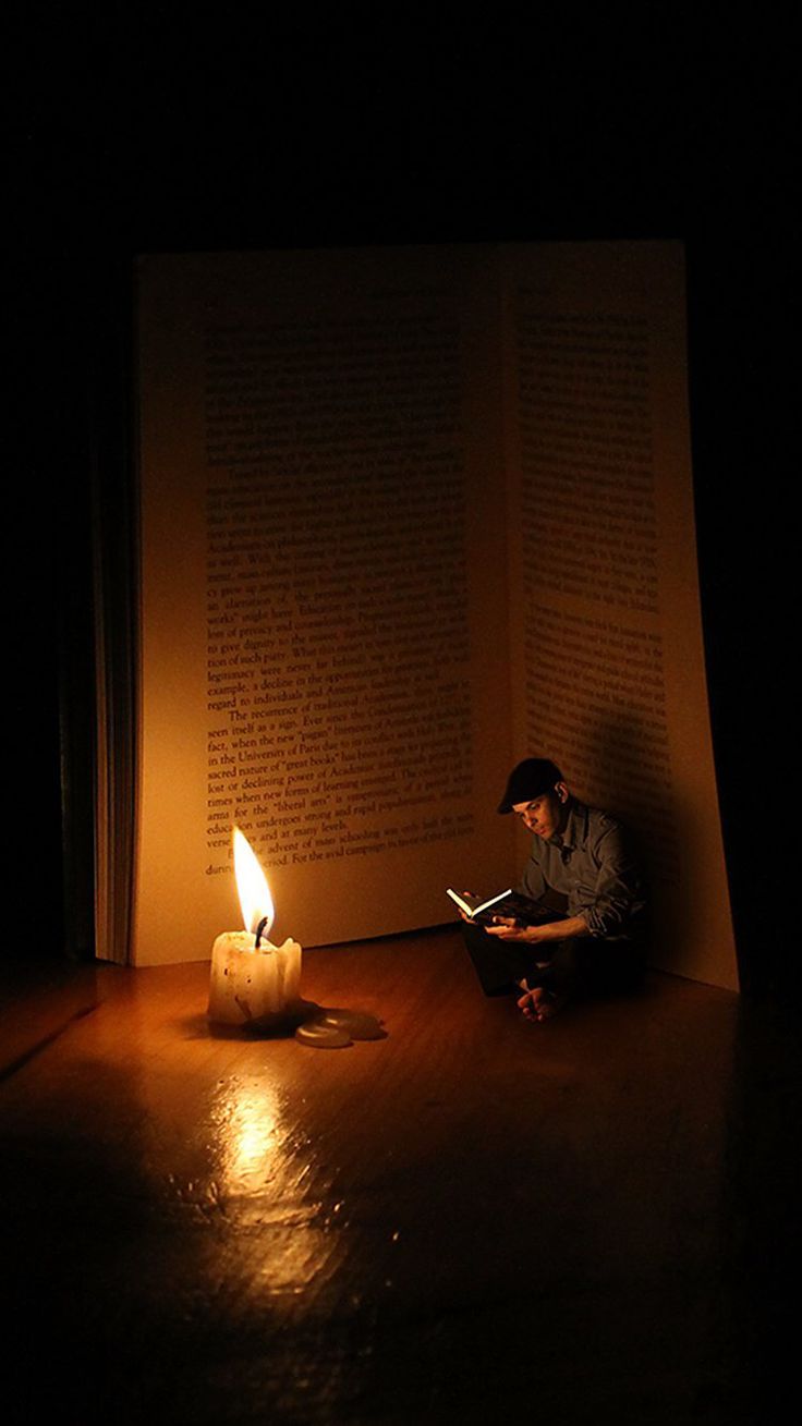 a man sitting on the floor reading a book with a lit candle in front of him