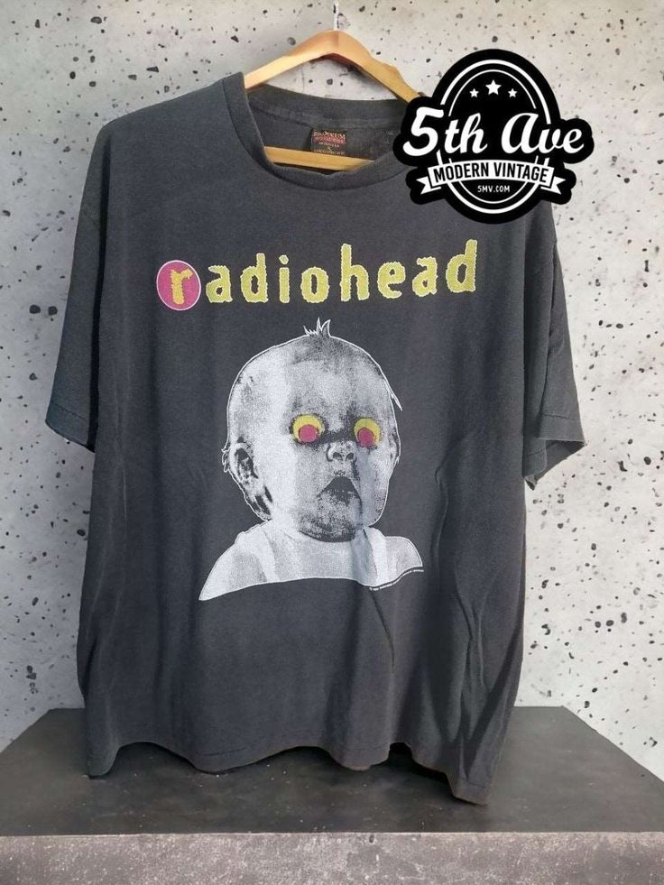 :his vintage-inspired Radiohead t shirt is made from 100% cotton, making it soft, breathable, and comfortable to wear. The black fabric is accented with a bold white print featuring the iconic Pablo Honey Tour logo, which showcases the band's name and tour details in a sleek, minimalist design. The shirt features a classic crew neck and short sleeves, making it a versatile option for any casual occasion. It is expertly crafted with a single stitch construction, creating a clean and streamlined look that is both durable and timeless. This technique involves using a single thread to sew the seams of the shirt, resulting in a smooth finish without any extra bulk or excess fabric. The Radiohead Pablo Honey Tour t shirt is a must-have for any true fan of the band or collector of vintage concert Washed Black Band Merch T-shirt With Graphic Print, Vintage Graphic Print T-shirt For Alternative Fashion, Vintage Washed Black T-shirt For Concert, Alternative Style Washed Black Graphic T-shirt, Band Merch T-shirt In Washed Black For Streetwear, Retro Black T-shirt For Concert, Band Merch T-shirt In Washed Black For Concert, Acid Wash Alternative Style T-shirt With Screen Print, Vintage Style Short Sleeve T-shirt