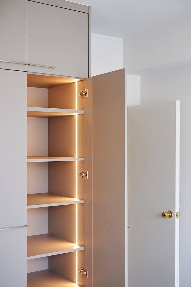 an open closet with several shelves and lights on the door, in front of a white wall