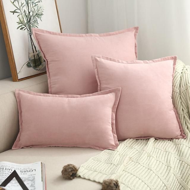 three pink pillows sitting on top of a white couch next to a book and plant