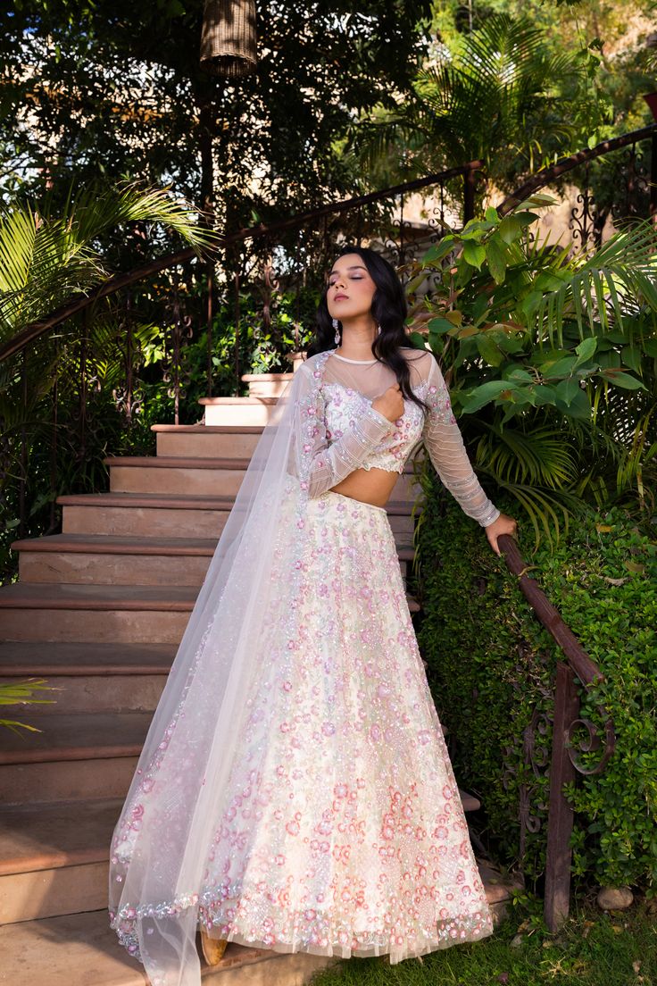 Elevate your wardrobe with this exquisite Suruchi Parakh Off-White Net Embroidered Lehenga Set. Crafted from delicate net fabric, this set features intricate handwork that adds a touch of elegance and sophistication to the entire outfit.
The off-white lehenga is paired with a matching blouse and a dupatta, creating a cohesive and harmonious look. The blouse has a classic round neckline and half sleeves, and the dupatta drapes beautifully on the body, enhancing your curves and adding a touch of g Bollywood Style White Ceremony Dress, White Gown With Resham Embroidery For Ceremony, White Dress With Zari Work For Ceremony, Off White Organza Sets For Reception, Floor-length Sets With Floral Embroidery For Ceremony, Floor-length Ceremony Sets With Floral Embroidery, White Gown With Zari Work For Ceremony, White Gown With Dupatta For Ceremony, White Gown With Traditional Drape For Ceremony