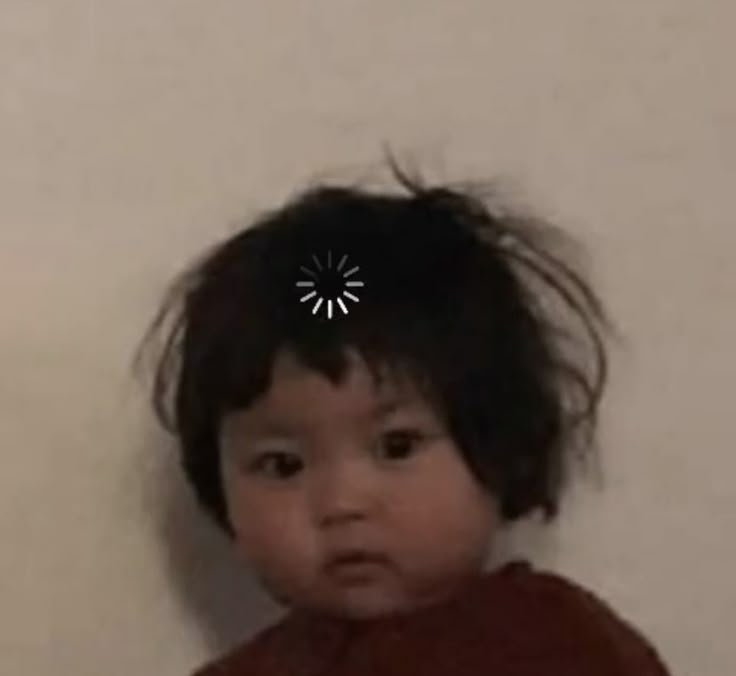 a young child with black hair standing in front of a wall and looking at the camera