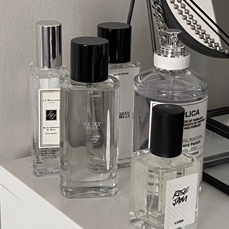 three bottles of perfume sitting on top of a white counter next to a mirror and lamp