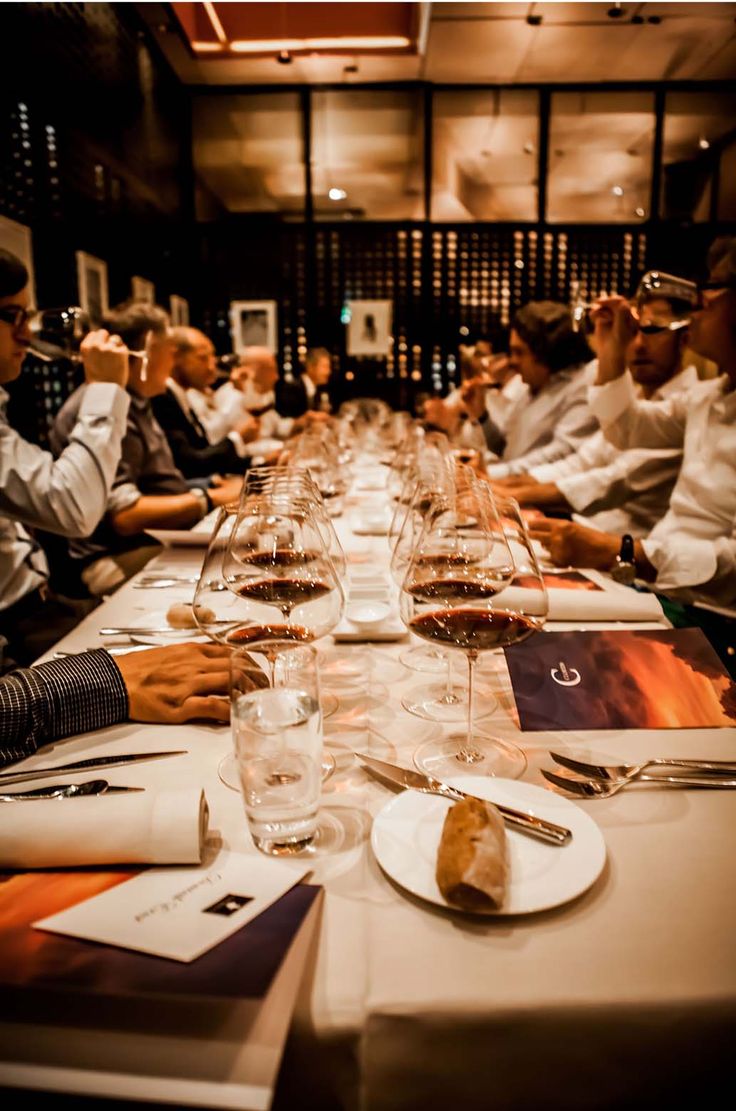 many people are sitting at a long table with wine glasses