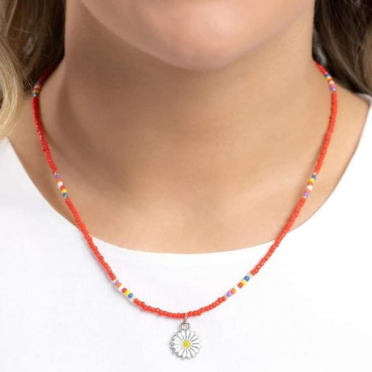 a woman wearing a red beaded necklace with a white flower charm on it's end