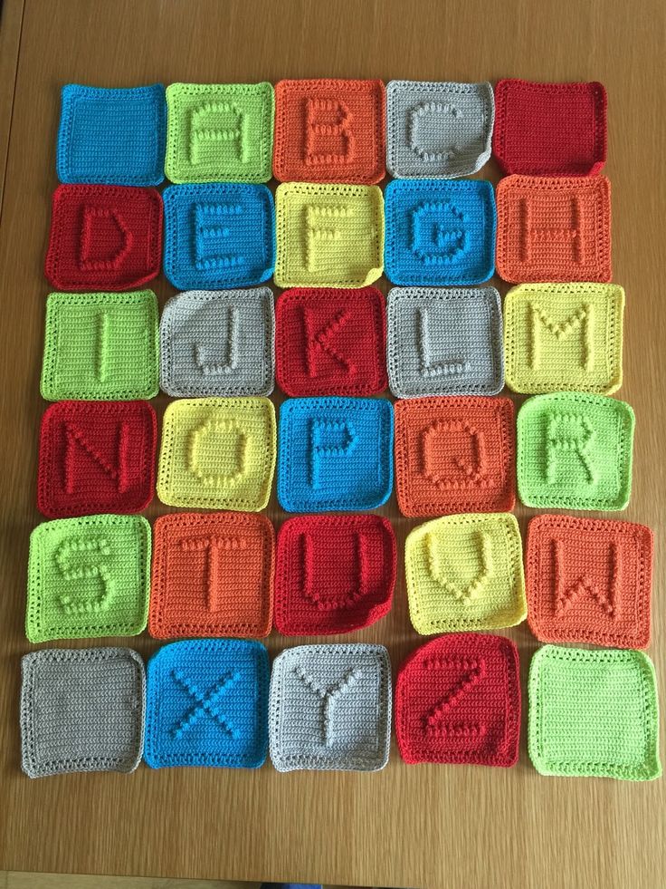 crocheted squares with letters and numbers are arranged on a wooden table, including one for each letter