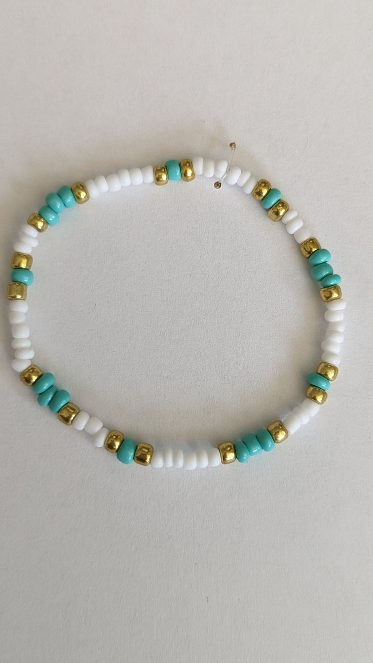 a white and blue beaded bracelet with gold accents on it's end, against a white background