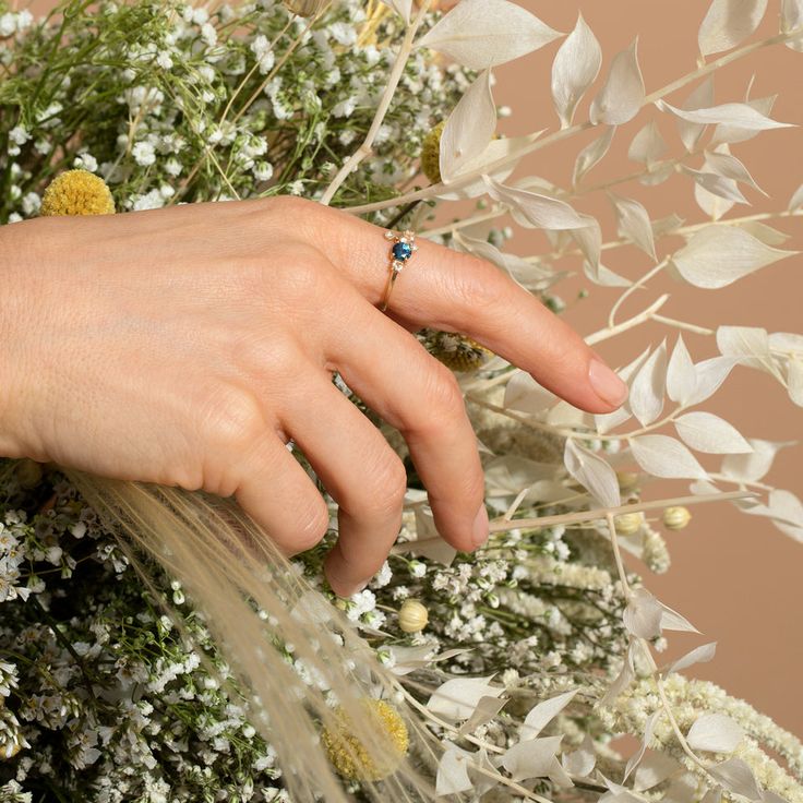 a woman's hand on top of a bouquet of flowers with a blue diamond ring