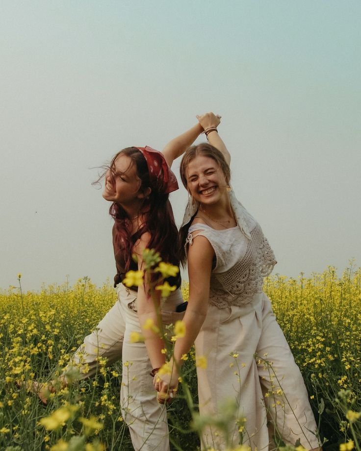 two girls are standing in a field with yellow flowers and one girl has her arm around the other