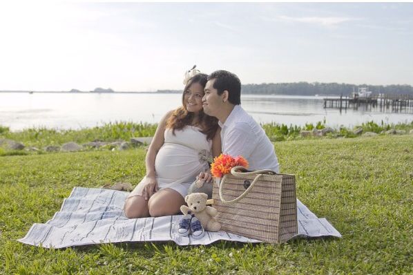 a man and woman are sitting on the grass with a teddy bear