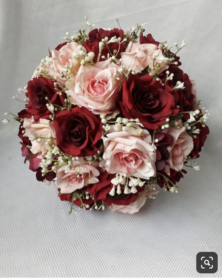 a bouquet of red and pink flowers on a white background with baby's breath