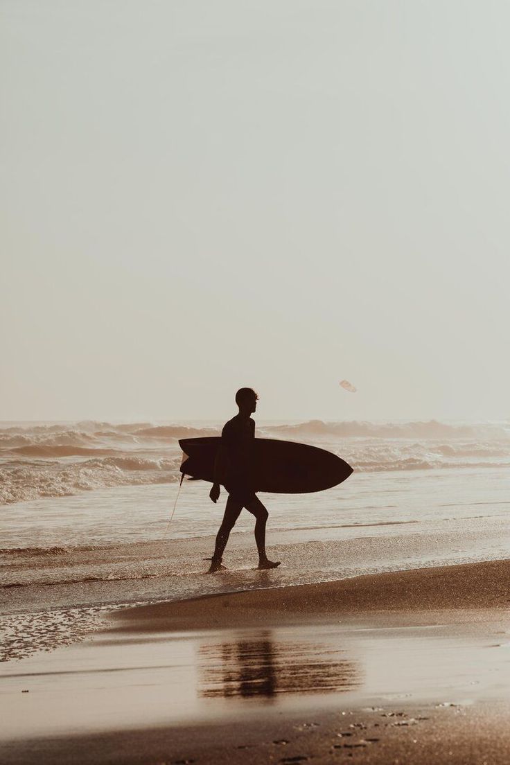 a person walking on the beach with a surfboard in their hand and water behind them