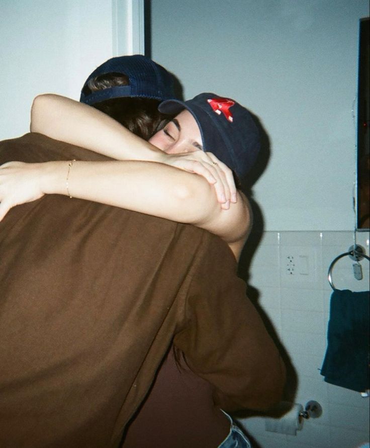 two people hugging each other in the bathroom while one person is wearing a beanie