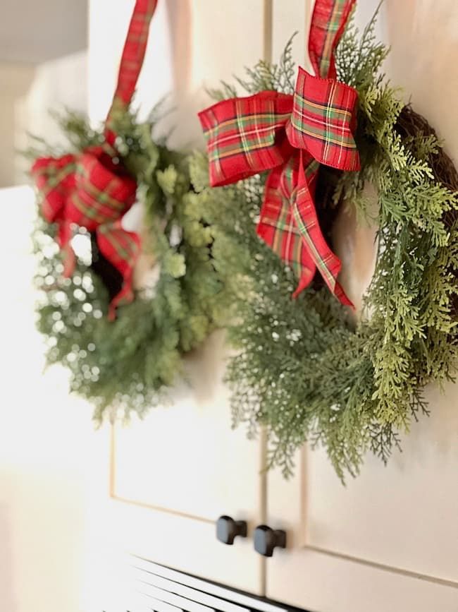 two wreaths hanging on the wall with red and green bows attached to them,