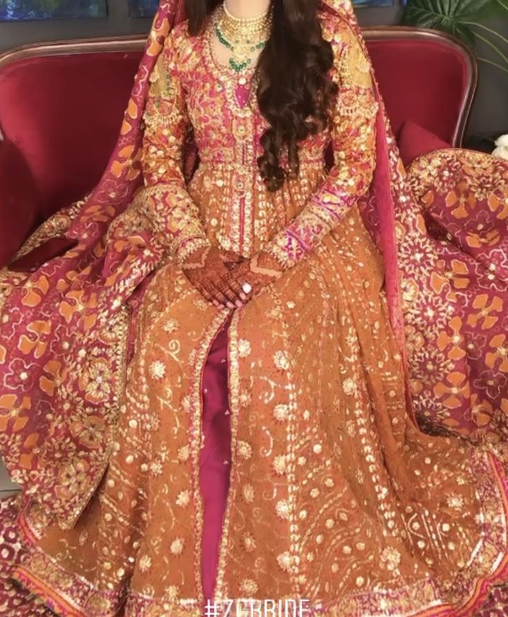 a woman sitting on top of a red couch wearing a brown and pink dress with gold accents