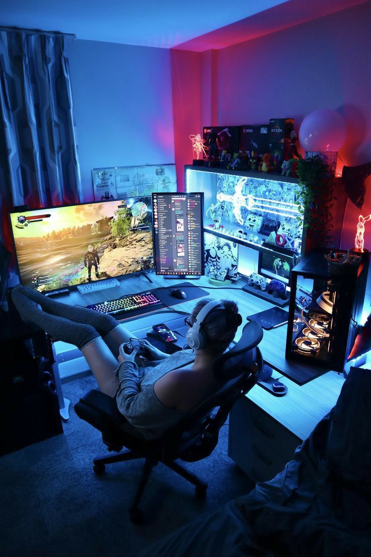 a man sitting in front of a computer desk with two monitors on it and a game controller